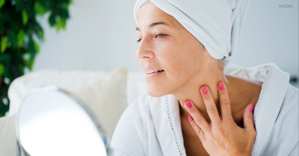 Woman (model) examining her chin and neck in the mirror.