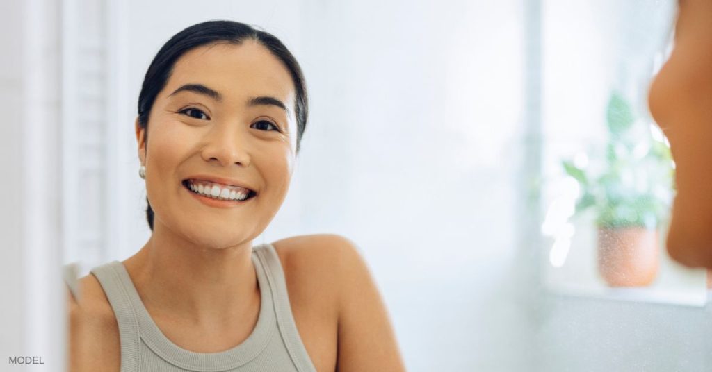 Woman (model) looking in the mirror and smiling.